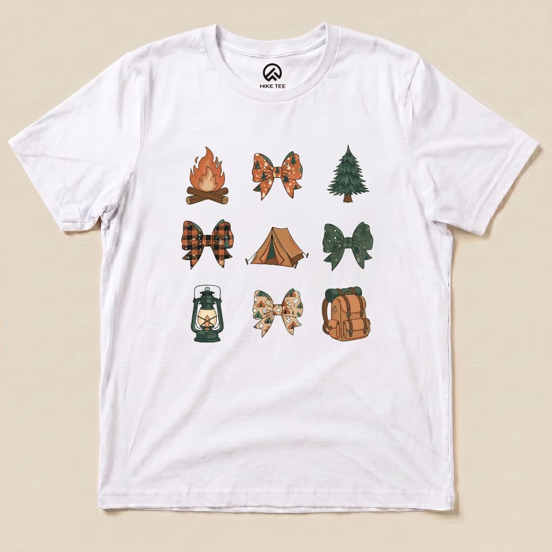 The Camping Bows Shirt features a white graphic t-shirt adorned with various camp-themed bows, a campfire, lantern, tent, and tree designs.