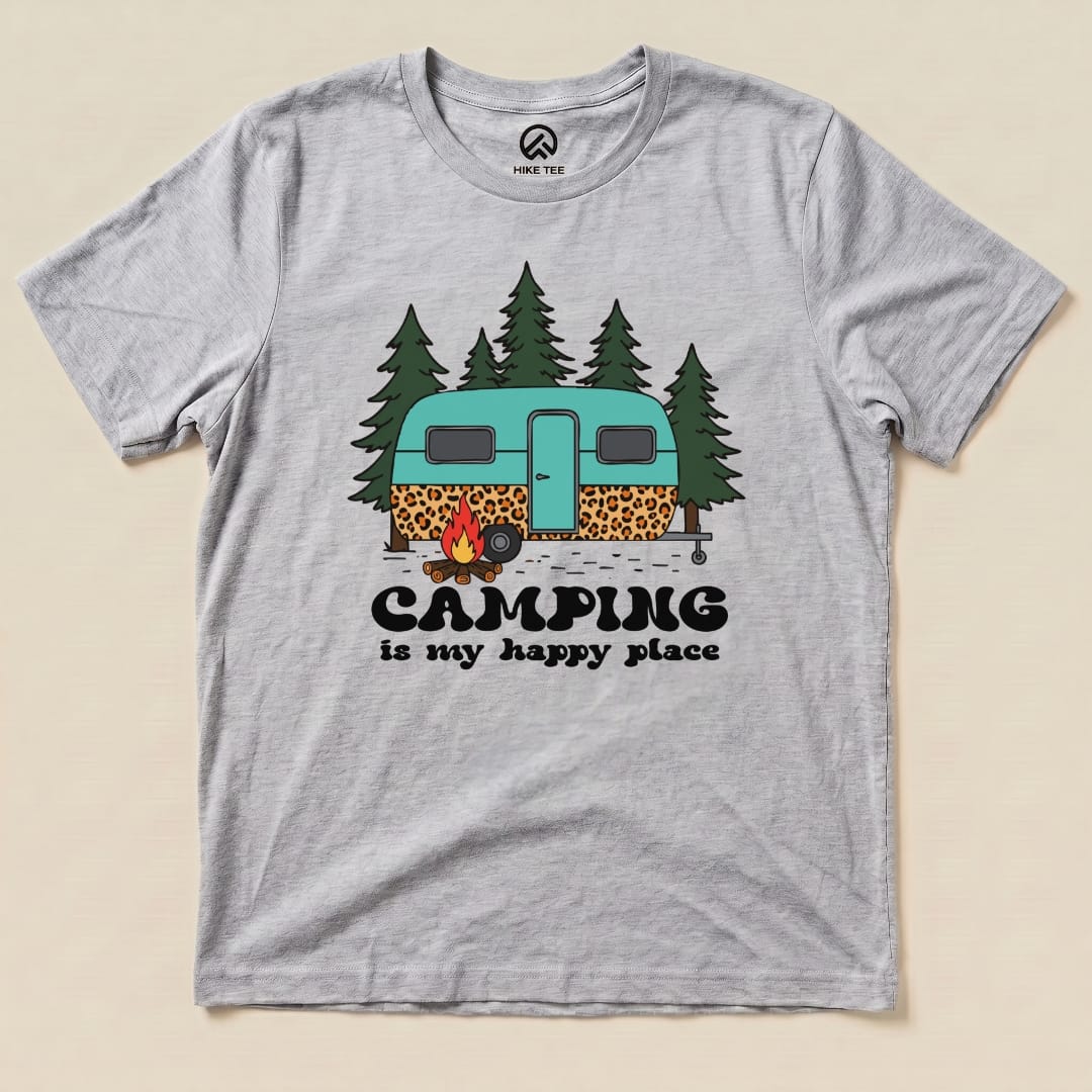A gray graphic t-shirt features a colorful illustration of a retro camper surrounded by trees and the slogan "Camping is my happy place.