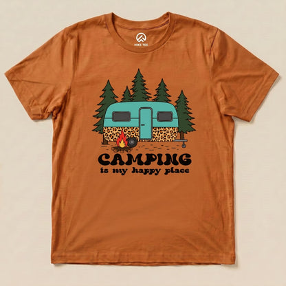 A flat graphic t-shirt in orange featuring a vintage trailer, campfire, trees, and the slogan "Camping is my happy place.