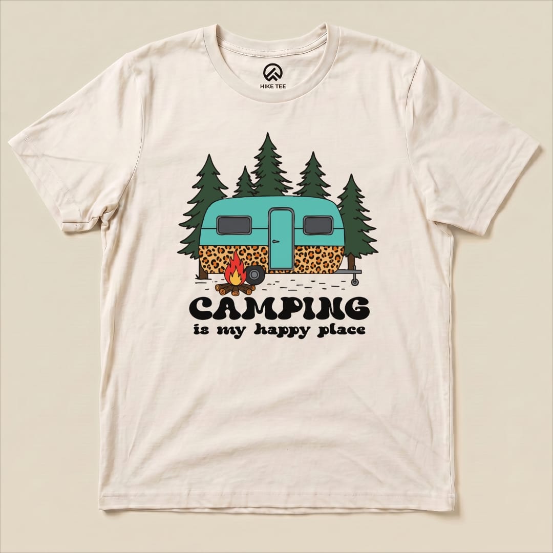 A graphic t-shirt featuring a teal camper surrounded by trees and a campfire, with the slogan "Camping is my happy place.