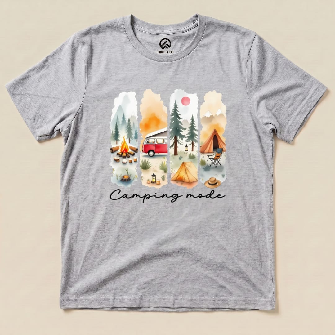 A gray graphic t-shirt featuring a vibrant watercolor design of camping scenes with the phrase "Camping mode" prominently displayed.