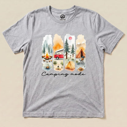 A gray graphic t-shirt featuring a vibrant watercolor design of camping scenes with the phrase "Camping mode" prominently displayed.