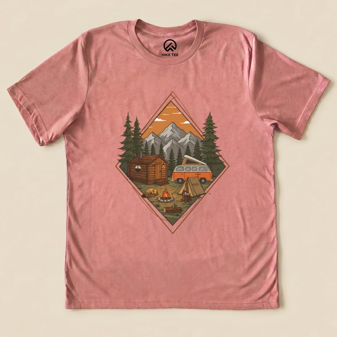 A pink graphic t-shirt featuring a Camping Scenery Shirt design with a cabin, campfire, tent, and vintage van against a mountain backdrop.
