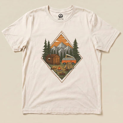 A graphic t-shirt featuring a detailed camping scenery design with a cabin, camper van, trees, and a campfire.