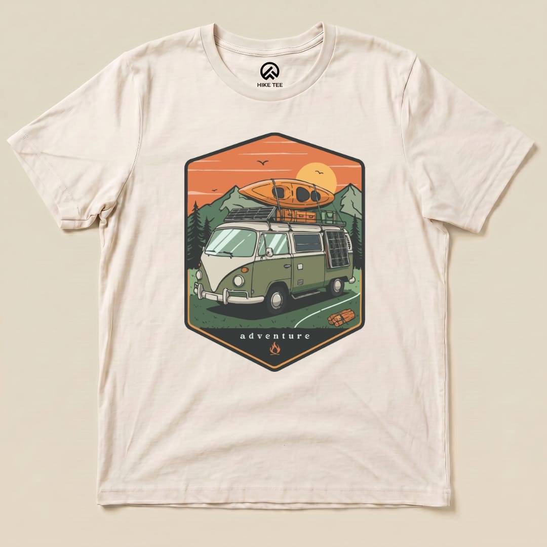 A graphic t-shirt featuring a camping van with a kayak on top, surrounded by mountains and the word "adventure" below.