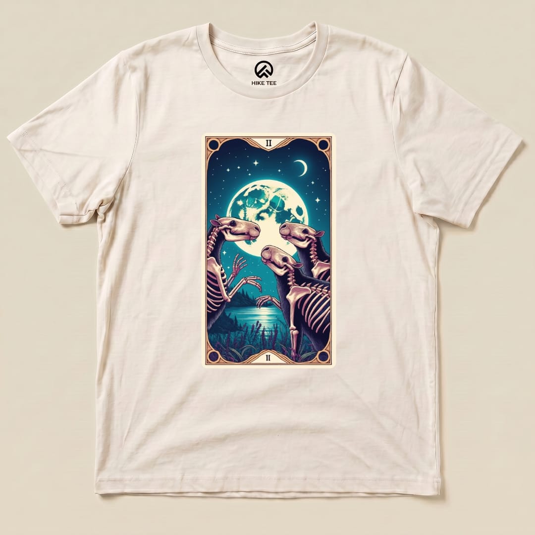 A graphic t-shirt featuring a whimsical design of skeletal capybaras and a full moon, titled "Capybara Moon Tarot Card Shirt.