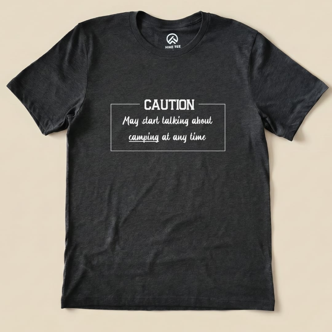 Graphic t-shirt in dark gray featuring the text "Caution May start talking about camping at any time" in a playful font.