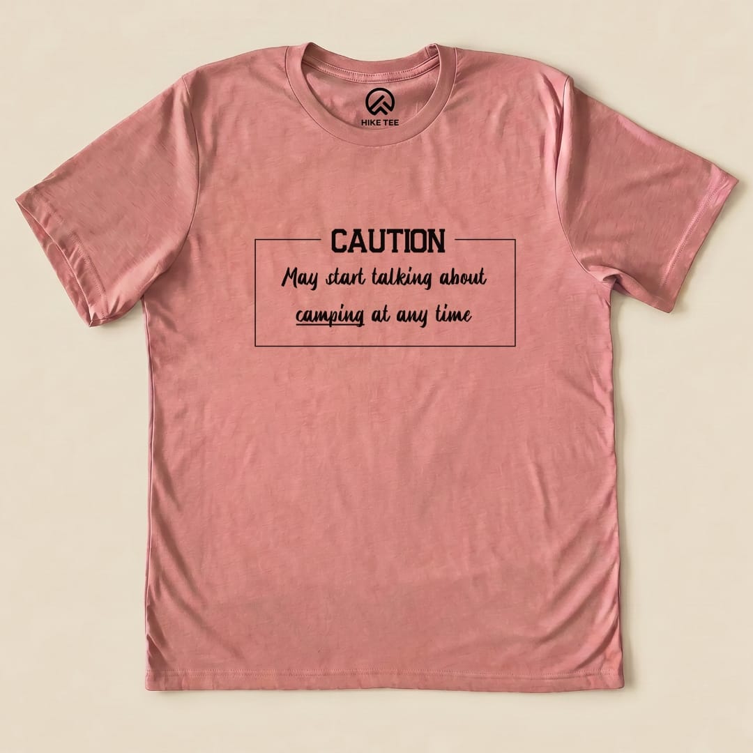 A flat graphic t-shirt in soft pink showcases the text "Caution May start talking about camping at any time" prominently.