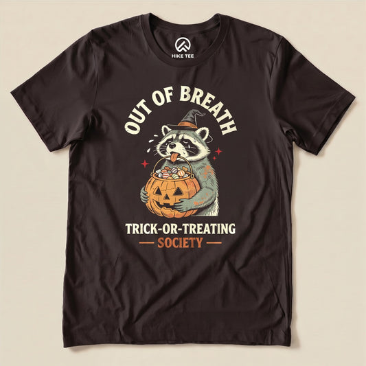 Brown Out of Breath Trick-or-Treating Society Shirt with a raccoon witch holding a pumpkin full of candy graphic