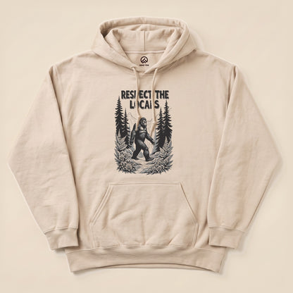 A beige hoodie features a graphic of Bigfoot walking through a forest with the text "Respect The Locals Bigfoot Hoodie".