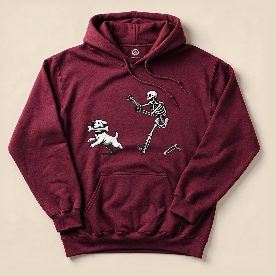 A maroon Skeleton and Dog Hoodie features a playful graphic of a skeleton running with a dog holding a bone.