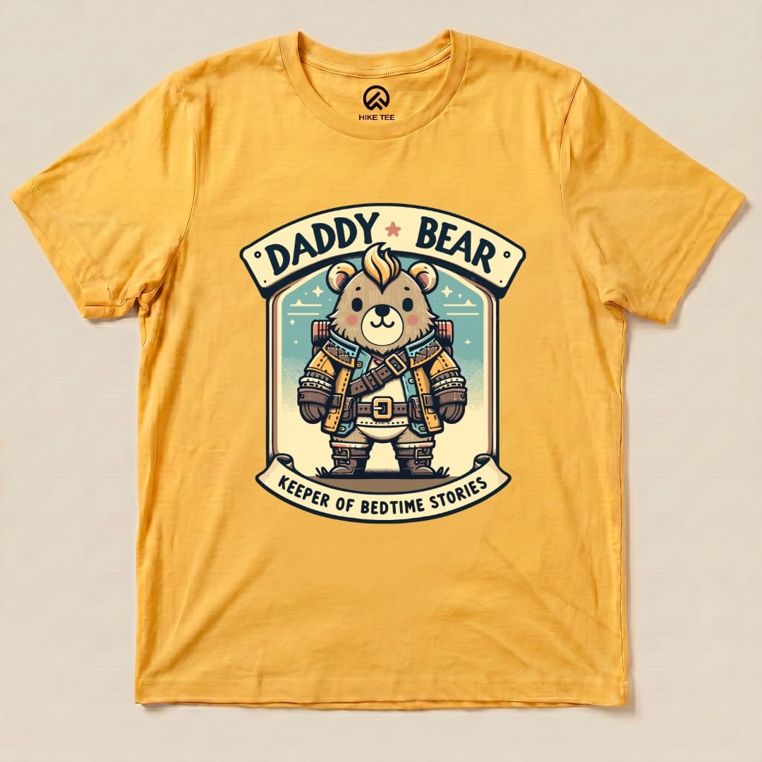 A yellow graphic t-shirt features a cartoon bear dressed as a rugged adventurer with the words "Daddy Bear" and "Keeper of Bedtime Stories.