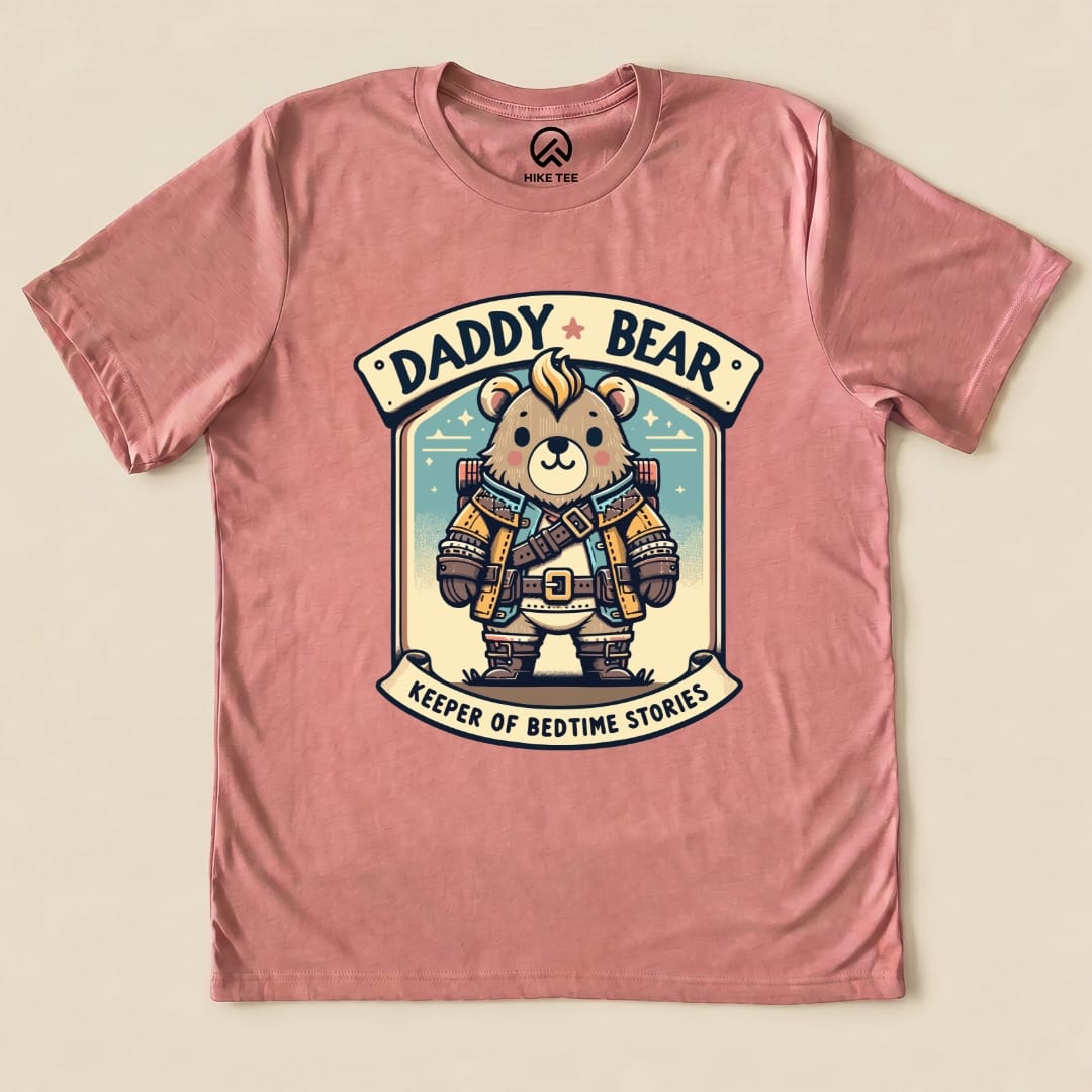 A graphic t-shirt in pink featuring a cartoon bear wearing a backpack and a belt, labeled "Daddy Bear, Keeper of Bedtime Stories.