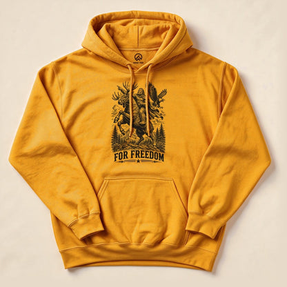 A close-up of a yellow Bigfoot Moose Resist Hoodie displaying a graphic of a moose and the slogan "FOR FREEDOM" surrounded by trees.