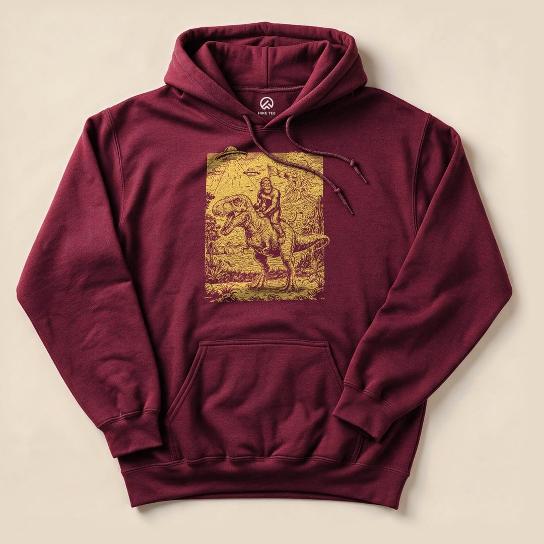 A maroon Bigfoot Dinosaur Hoodie featuring a graphic of Bigfoot riding a dinosaur in a forest setting.