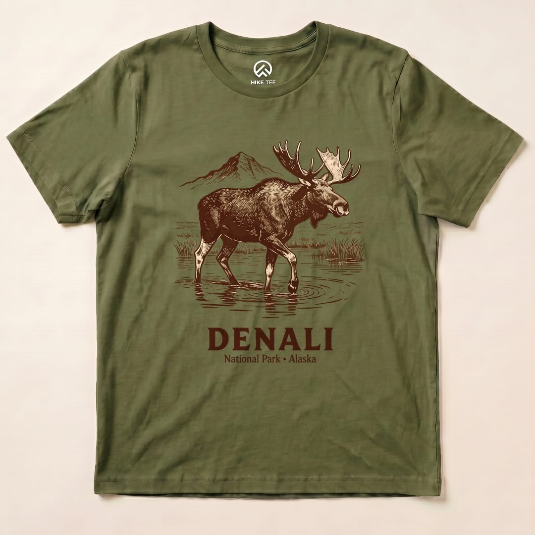 A graphic t-shirt featuring a moose wading in water with a mountain backdrop, reading "DENALI National Park - Alaska".