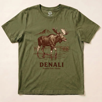 A graphic t-shirt featuring a moose wading in water with a mountain backdrop, reading "DENALI National Park - Alaska".