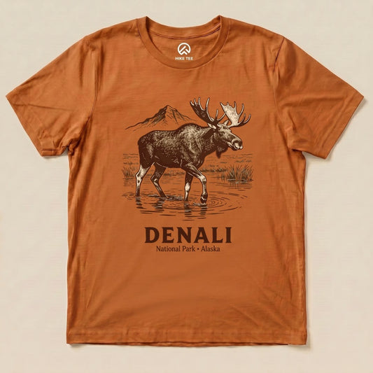 A graphic t-shirt featuring a moose standing in water with mountains in the background, labeled "Denali National Park Moose Shirt.