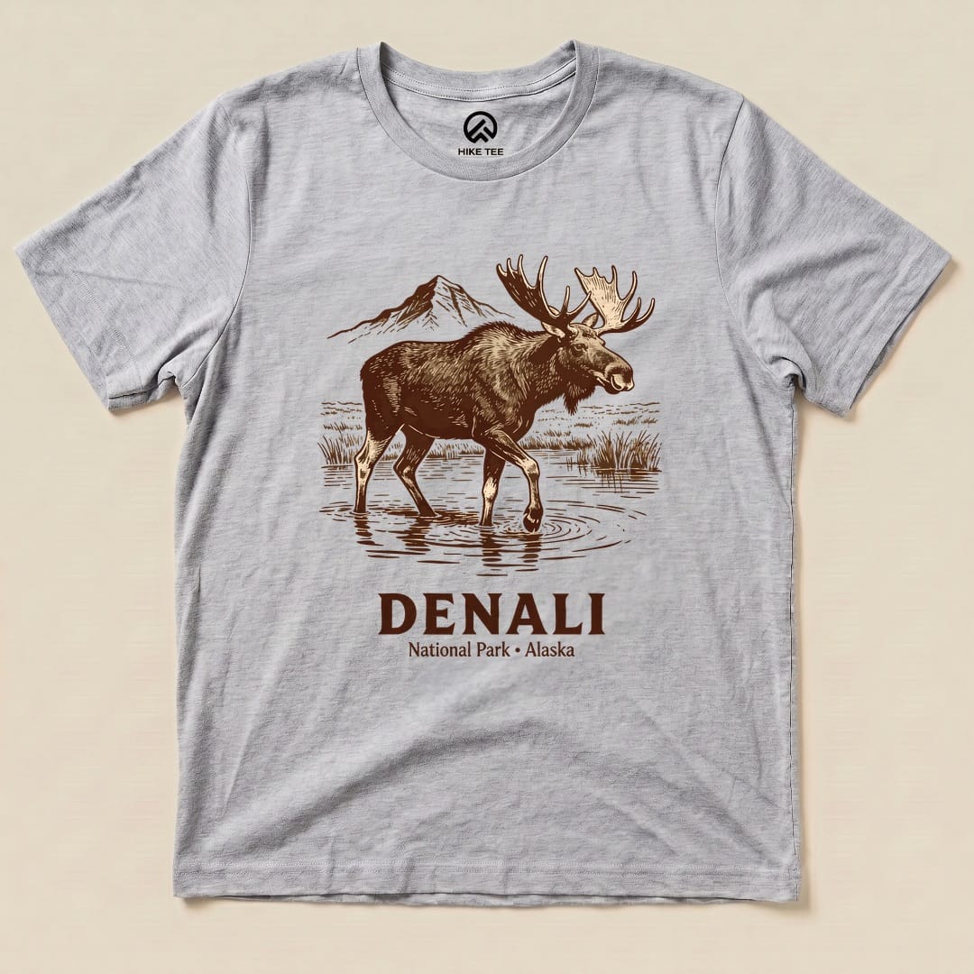 A graphic t-shirt featuring a moose standing in water with mountains in the background and the text "Denali National Park - Alaska.