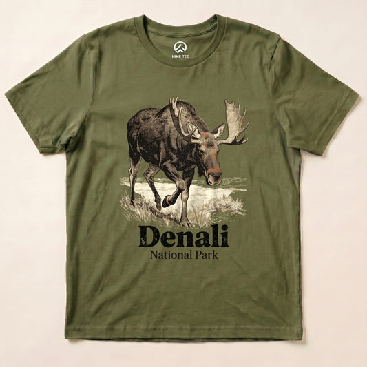 Graphic t-shirt featuring a moose illustration and the text "Denali National Park Shirt" in a stylish design on an olive green background.