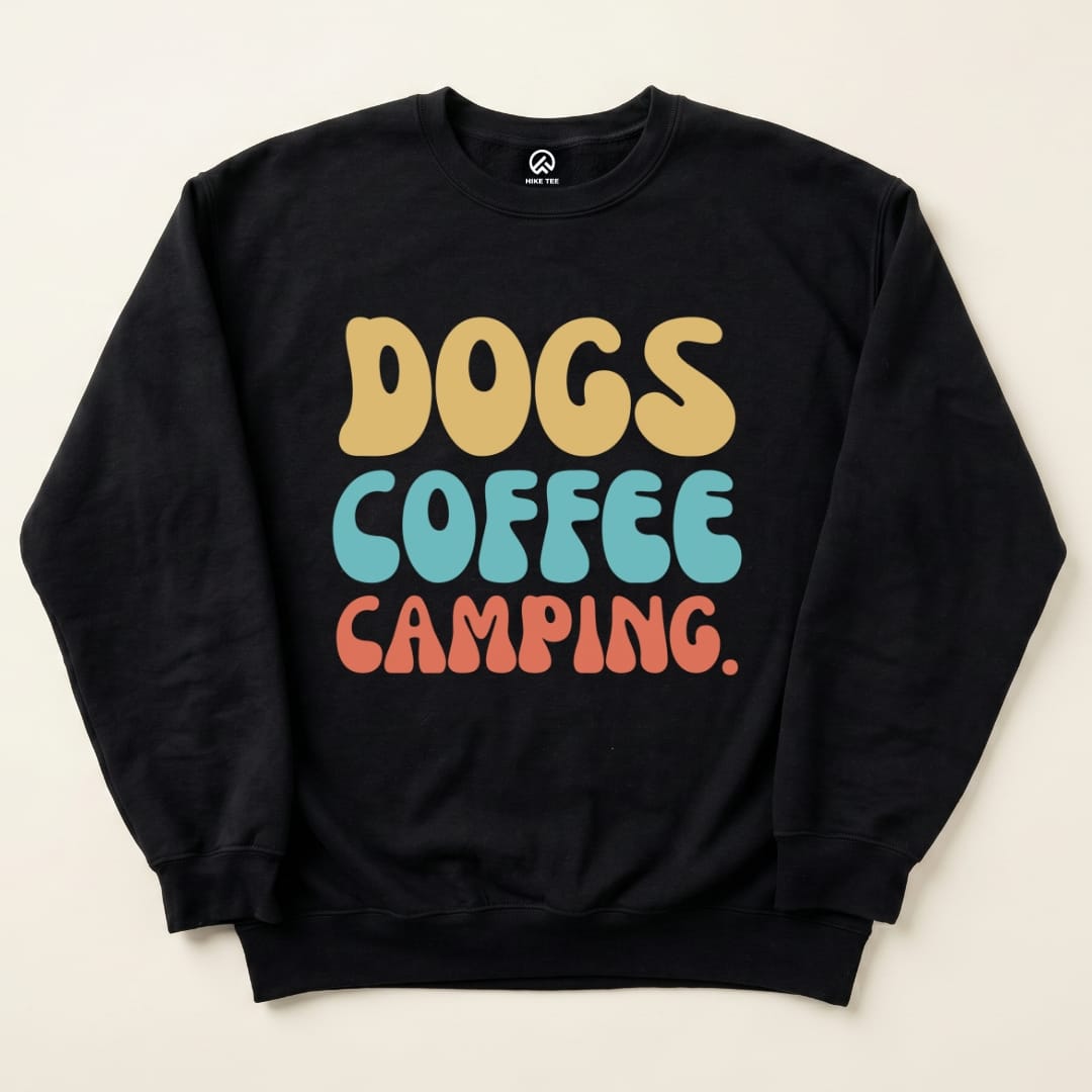 A black graphic t-shirt featuring colorful text that reads "DOGS COFFEE CAMPING" in a playful font.