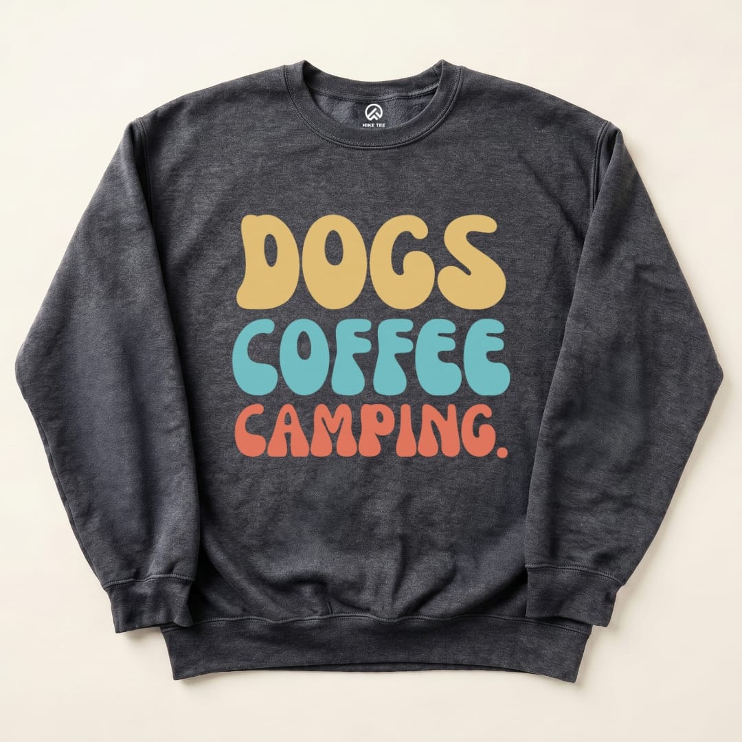 A graphic t-shirt featuring the playful text "DOGS COFFEE CAMPING" in vibrant colors on a dark background.