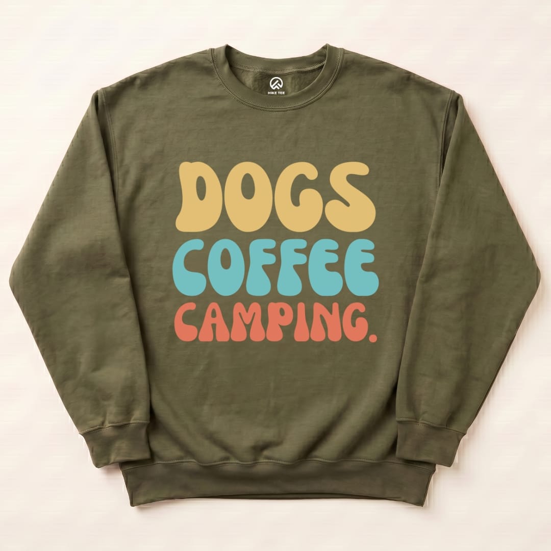 A graphic t-shirt in olive green featuring the playful slogan "DOGS COFFEE CAMPING" in colorful, retro lettering.