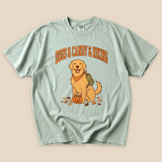 A mint green graphic t-shirt featuring a smiling golden retriever with a backpack and a pumpkin, stating "Dogs & Candy & Hiking.