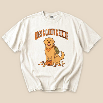 A graphic t-shirt featuring a smiling golden retriever with a pumpkin and the words "Dogs & Candy & Hiking" above in orange.