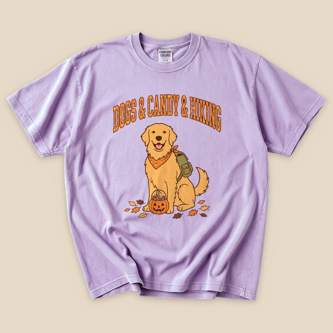 A lavender graphic t-shirt featuring a cheerful golden retriever with a backpack and a pumpkin, stating "Dogs & Candy & Hiking.