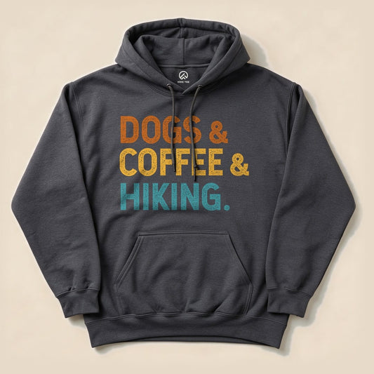 A dark gray hoodie featuring the phrase "Dogs & Coffee & Hiking." in vibrant orange and teal letters, showcasing a fun outdoor theme.