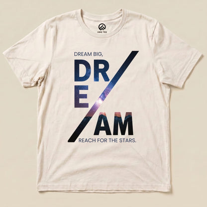 A graphic t-shirt featuring the text "DREAM BIG, DREAM REACH FOR THE STARS" with a starry background on a light fabric.