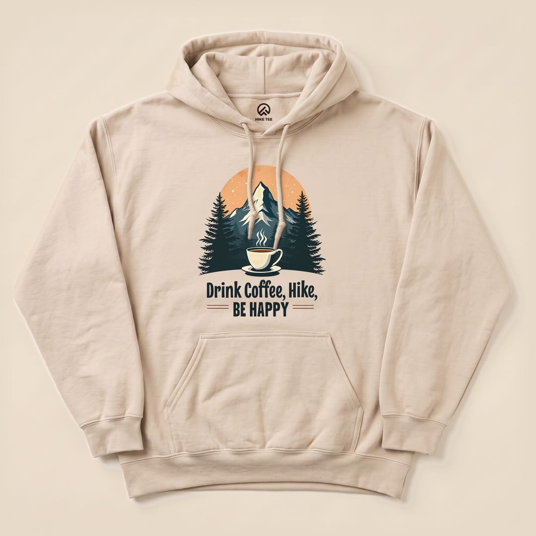 A beige hoodie featuring a graphic design of a coffee cup, mountains, and the slogan "Drink Coffee, Hike, Be Happy.