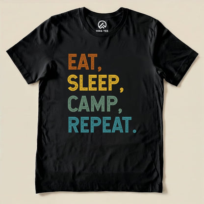 A black graphic t-shirt features the phrase "Eat Sleep Camp Repeat" in vibrant, multi-colored text.