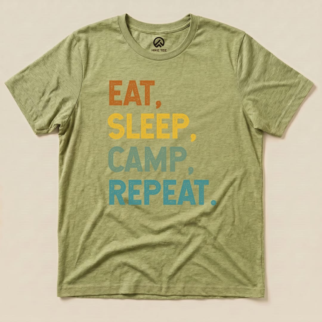 A flat olive green graphic t-shirt featuring the slogan "Eat, Sleep, Camp, Repeat" in bold, colorful letters.