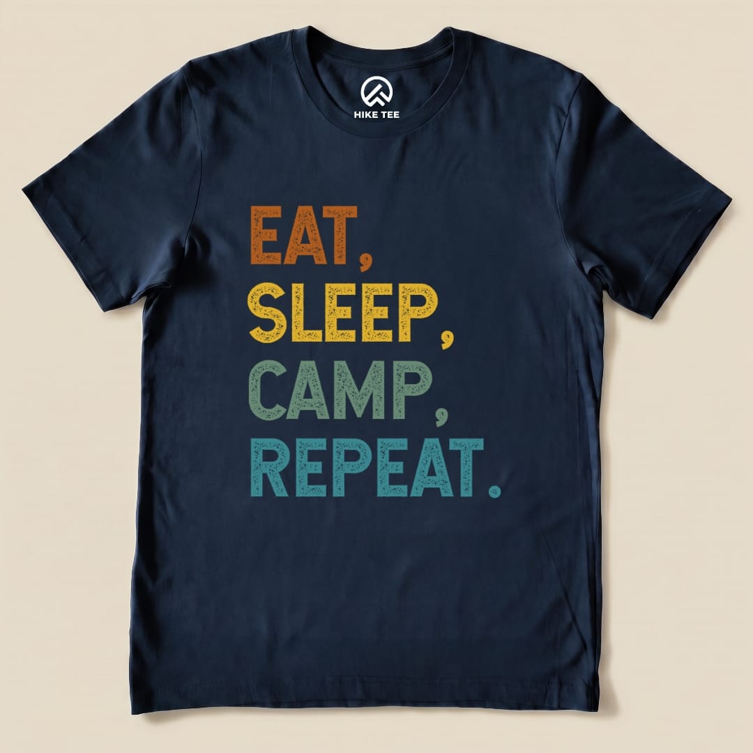 A navy graphic t-shirt featuring the phrase "Eat, Sleep, Camp, Repeat" in colorful, textured lettering.