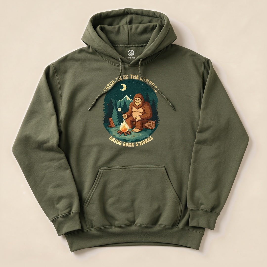 Olive green "Bring Some Smores Hoodie" featuring a graphic of Bigfoot roasting marshmallows by a campfire in a forest.