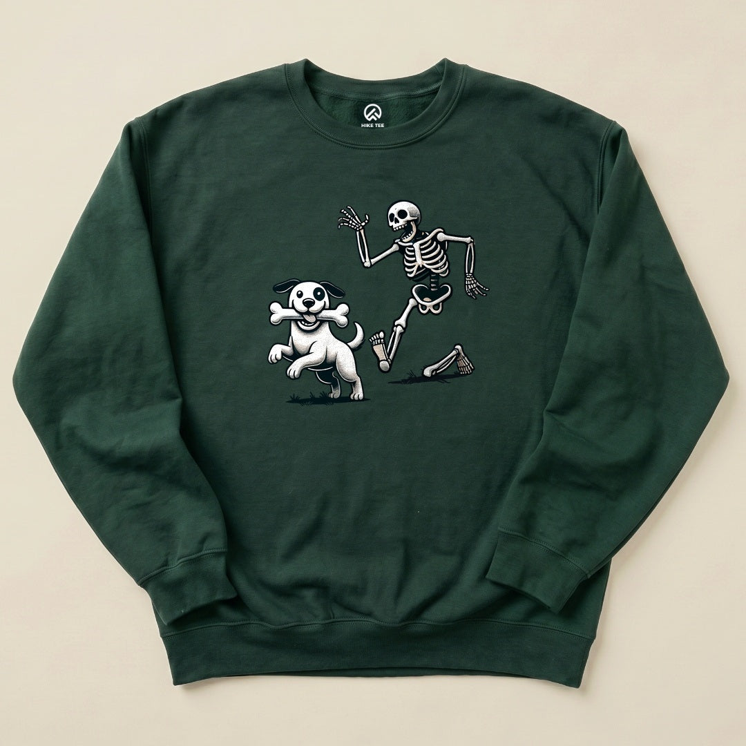 Graphic t-shirt featuring a playful skeleton and dog, both in motion, with the skeleton waving, on a dark green background.