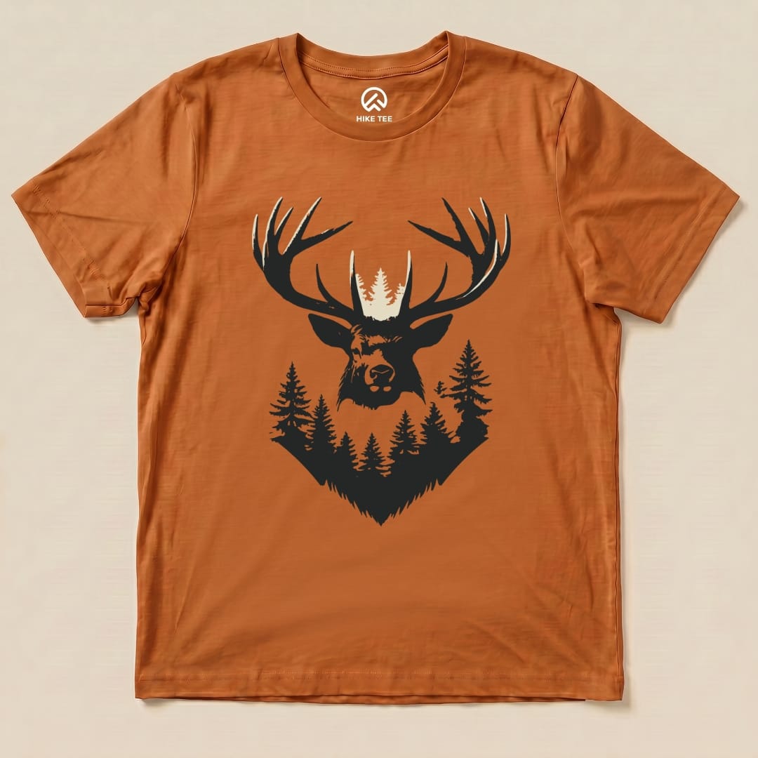 The Elk Shape Shirt is a graphic t-shirt featuring a striking dark elk head surrounded by trees, set against a warm orange background.