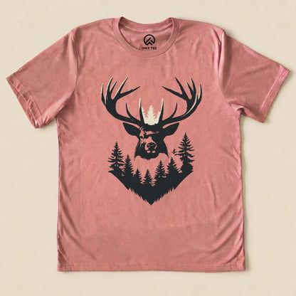 The Elk Shape Shirt features a bold graphic of an elk's head with antlers surrounded by trees, printed on a dusty rose t-shirt.