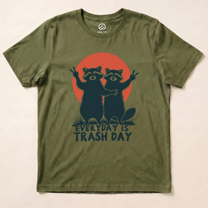 A flat olive green graphic t-shirt featuring two raccoons with a sunset background and the phrase "Everyday is Trash Day.