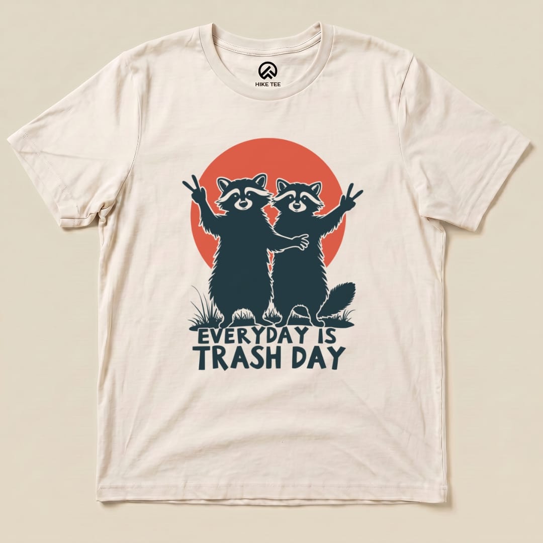 Graphic t-shirt featuring two raccoons with peace signs, a red sunset, and the slogan "Everyday is Trash Day.