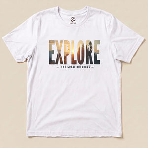 A white graphic t-shirt featuring the slogan "EXPLORE THE GREAT OUTDOORS" with a scenic mountain and sunset design.