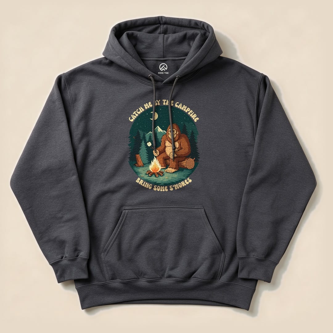 A dark gray hoodie featuring a graphic of a bear by a campfire with the slogan "Catch Me By The Campfire, Bring Some S'mores.
