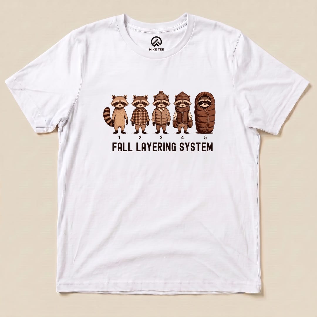 A graphic t-shirt featuring five raccoons in varying outfits with the text "FALL LAYERING SYSTEM" displayed below them.