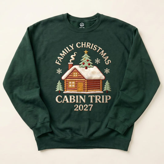 Forest Green Family Christmas Cabin Trip 2027 Sweatshirt with a snowy log cabin and Christmas tree graphic