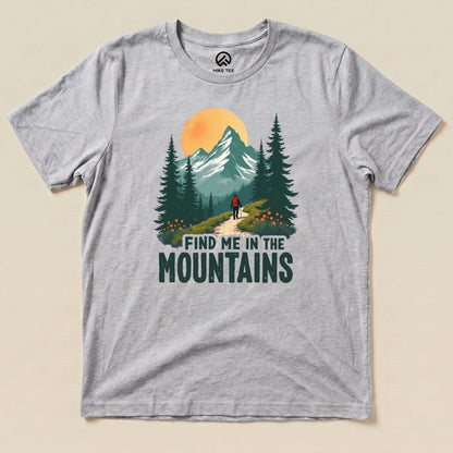 A gray graphic t-shirt displays the phrase "FIND ME IN THE MOUNTAINS" with an illustration of a hiker on a scenic mountain trail.