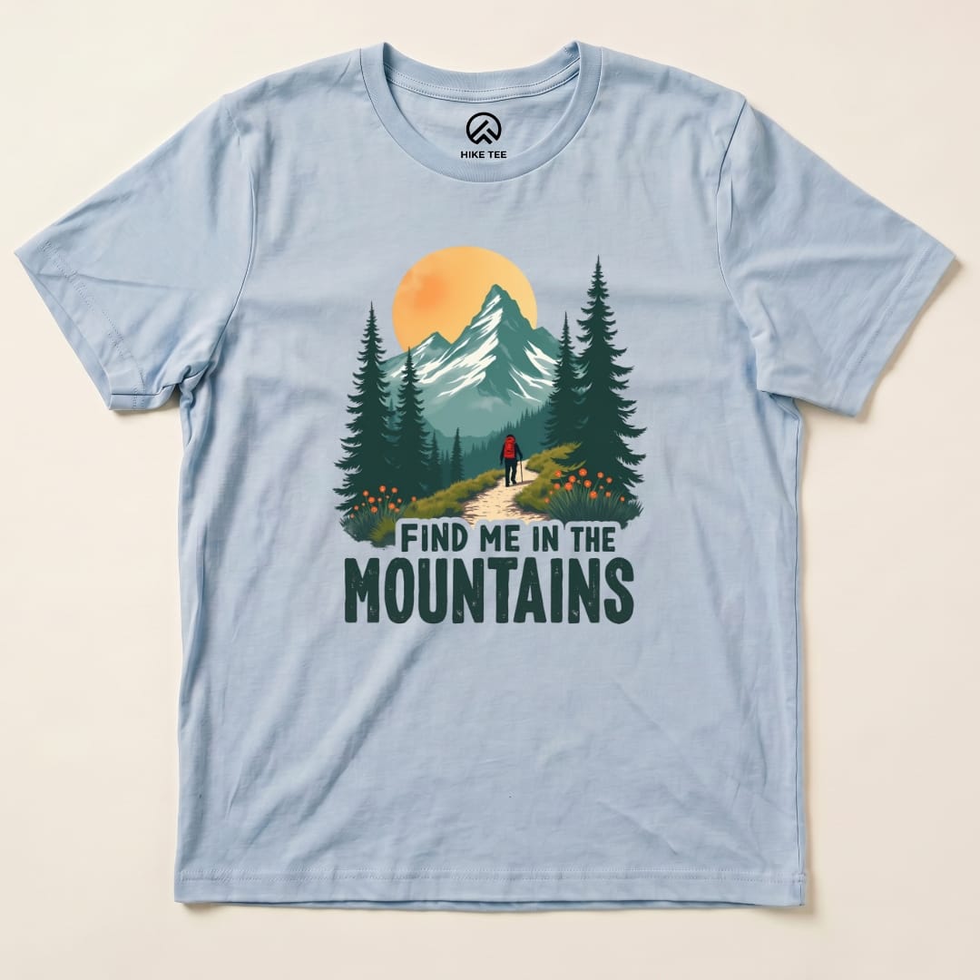 Graphic t-shirt featuring a nature scene with a hiker and the phrase "Find Me In The Mountains" under a colorful sunset.