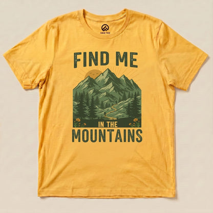 A graphic t-shirt in golden yellow featuring the phrase "Find Me In The Mountains" and a mountain landscape design.