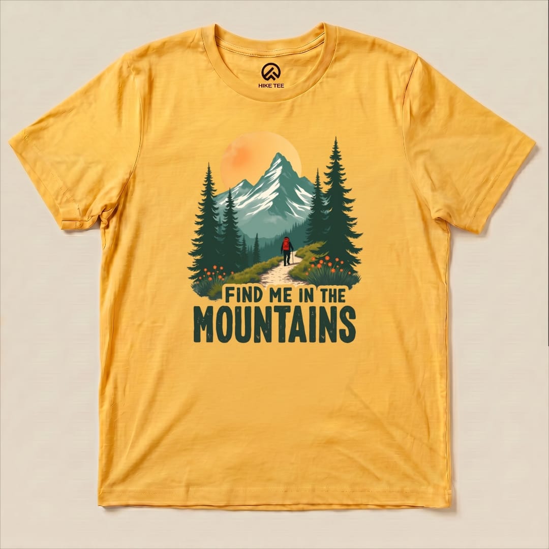 A yellow graphic t-shirt features a hiker on a trail surrounded by trees and mountains, with the text "Find Me In The Mountains.